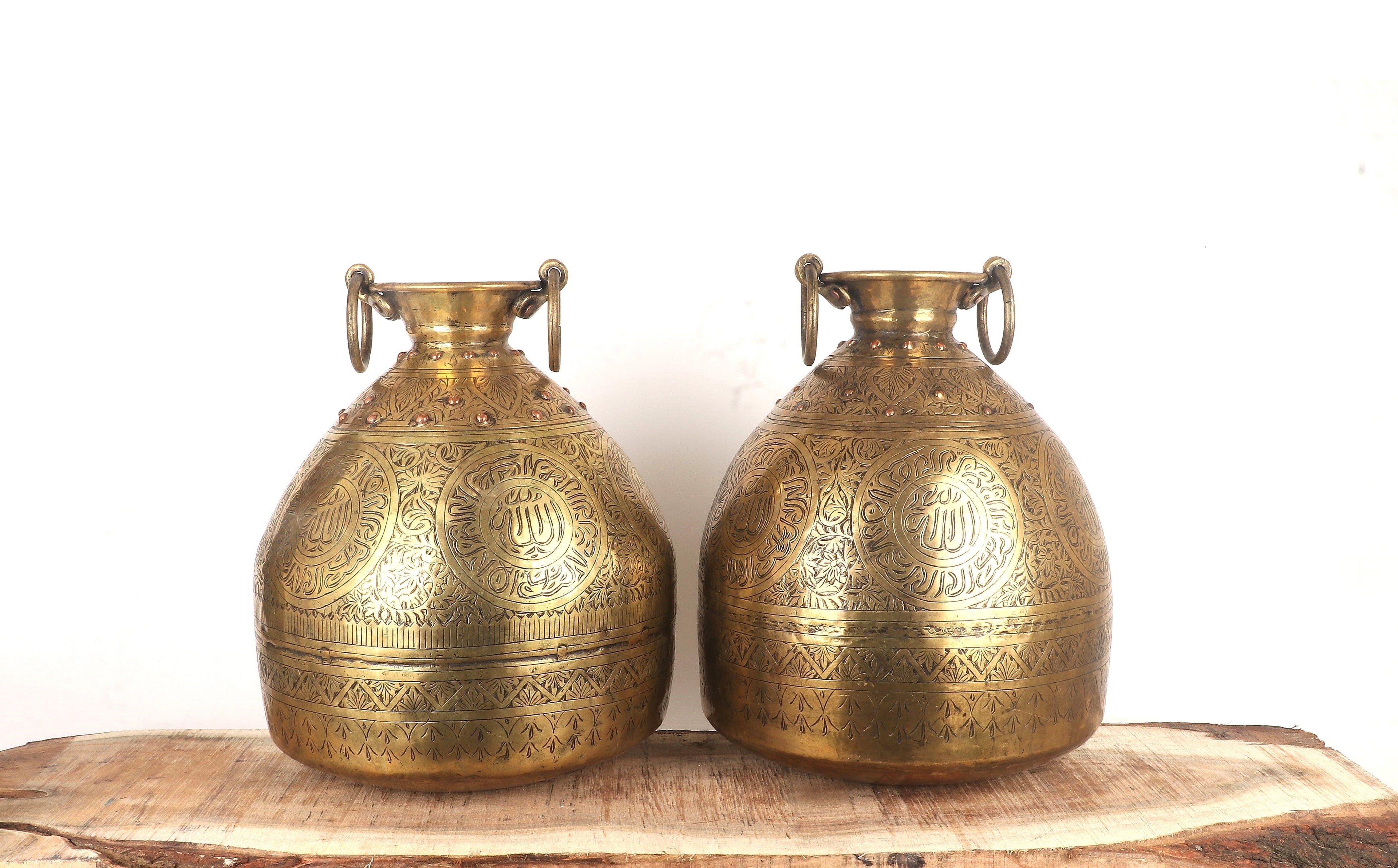 Two brass vases with intricate designs on a wooden surface.