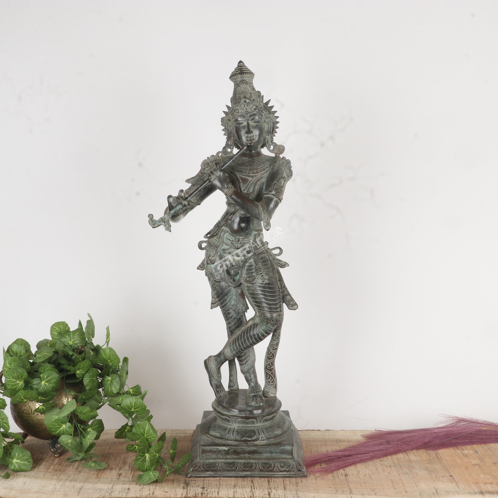 Bronze statue of a deity on a white background with greenery