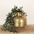 Decorative brass pot with plant on a wooden surface